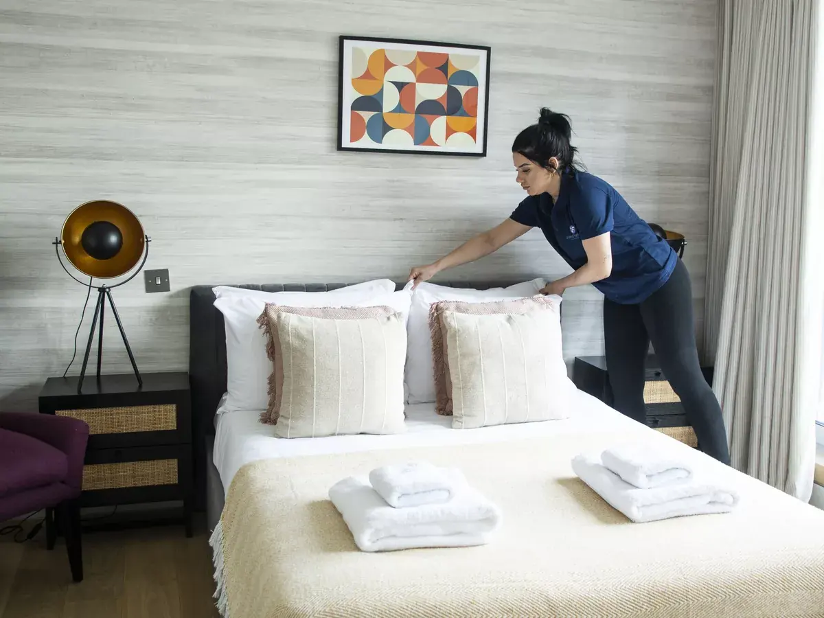 UF Cleaning housekeeper preparing a bright hotel bedroom