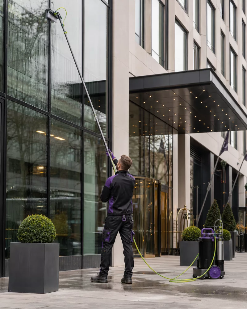 Professional window cleaner using a water-fed pole on a modern hotel exterior