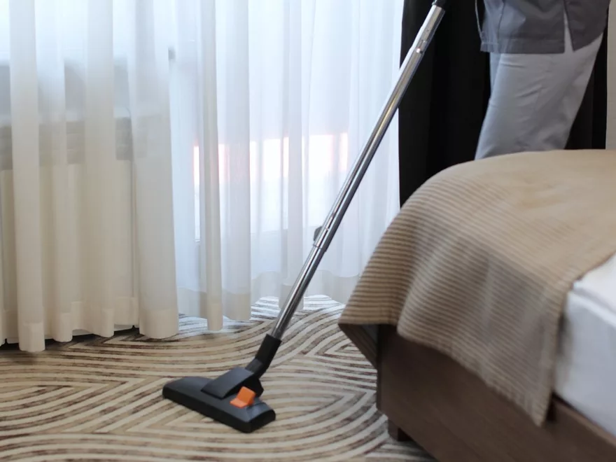 Housekeeper vacuuming the carpet beside a prepared guest bed
